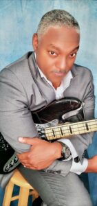 African American Bass Player siitng on a chair with his bass guitar with a blue background