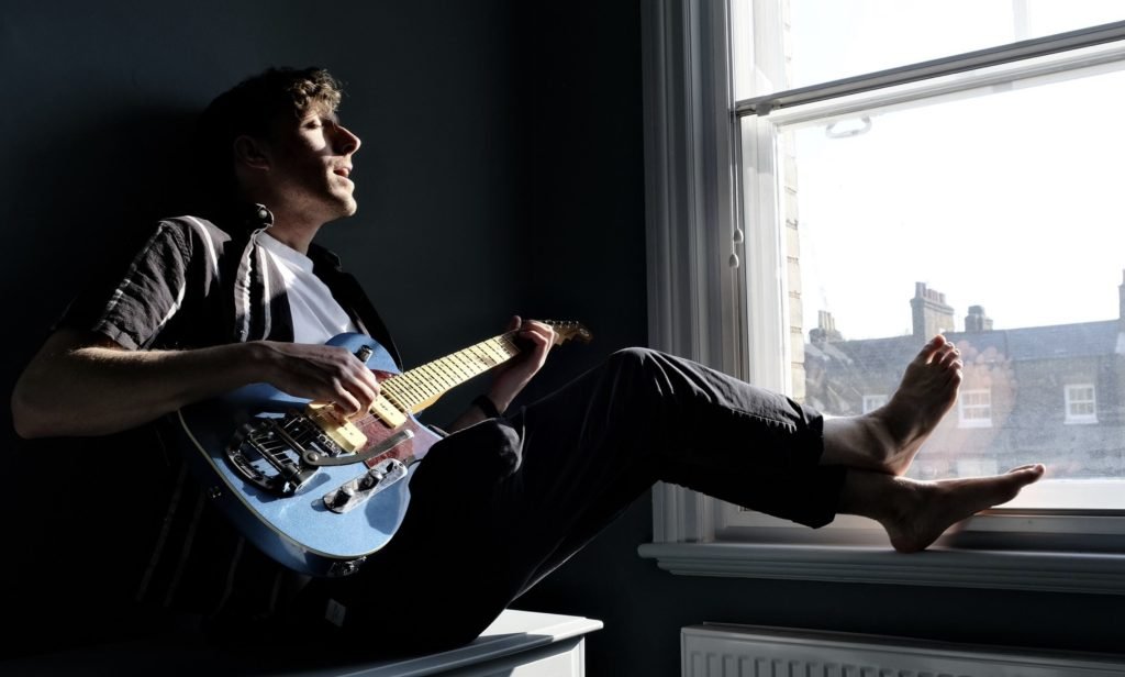 man sitting by the window playing the guitar