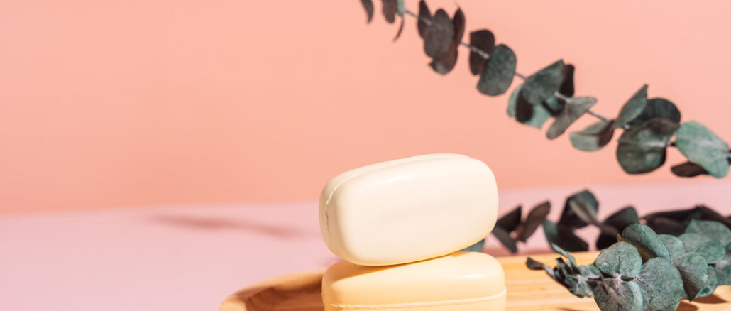 Two bars of soap in a wooden soap dish with dried flowers against a pink background.