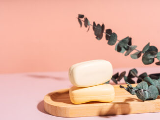 Two bars of soap in a wooden soap dish with dried flowers against a pink background.