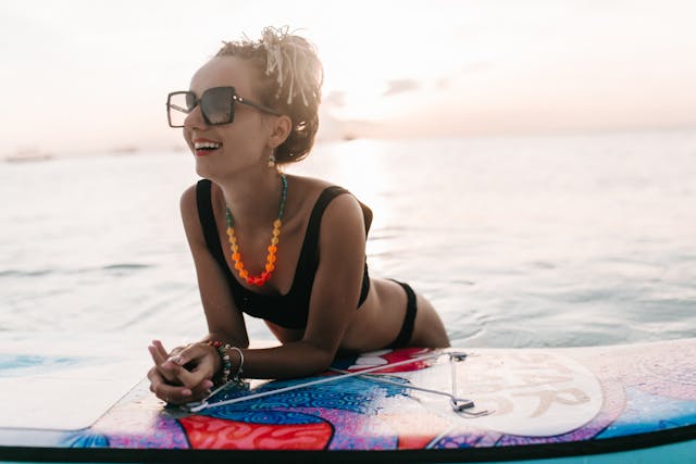 a woman wearing big bold sunglasses lying on a surfboard in the water