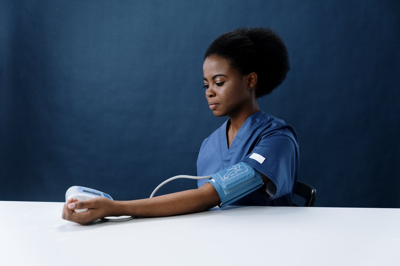 A healthcare professional in blue scrubs checking her blood pressure with a digital monitor, emphasizing the importance of managing high blood pressure.