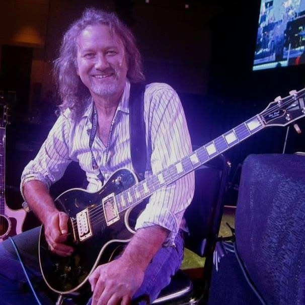 Josh Sklair, Grammy-winning guitarist, smiling while holding a black electric guitar during a live performance setup.