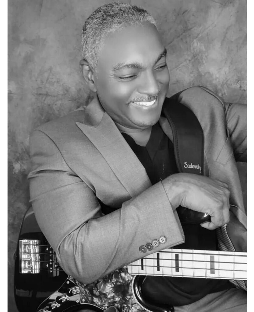 "Black and white photo of Mitchell Coleman Jr., Billboard-charting funk bassist, smiling while holding his Sadowsky bass guitar in a stylish suit