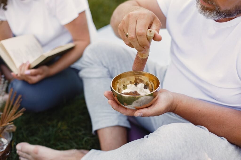 Person holding and playing a Tibetan singing bowl outdoors, surrounded by a peaceful atmosphere.