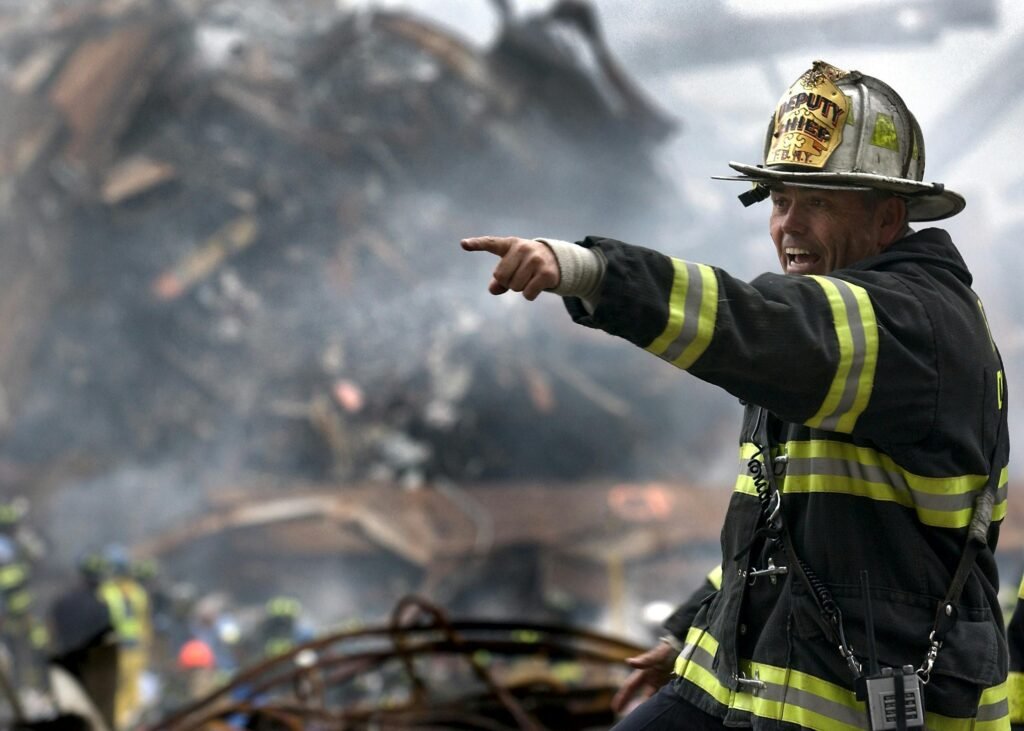 A firefighter in full gear directing efforts during the L.A. fire, with smoke and debris filling the background, showcasing urgency and leadership in crisis.