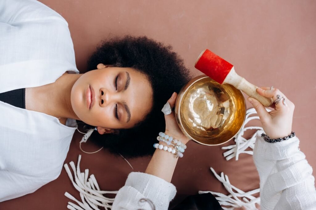 A woman lying down with closed eyes during a sound healing session using a Tibetan singing bowl, promoting relaxation and wellness.